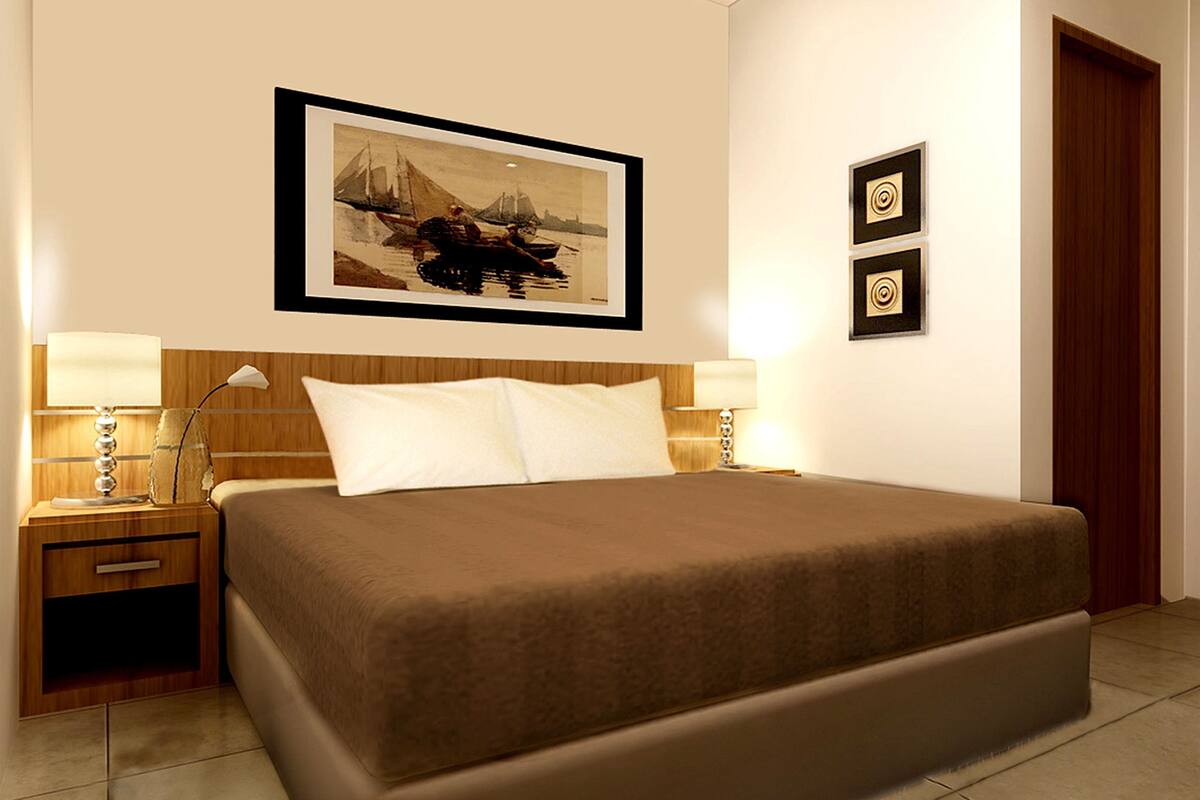 A neatly arranged hotel room with a large bed, two bedside tables with lamps, a framed picture on the wall, and a wooden door.