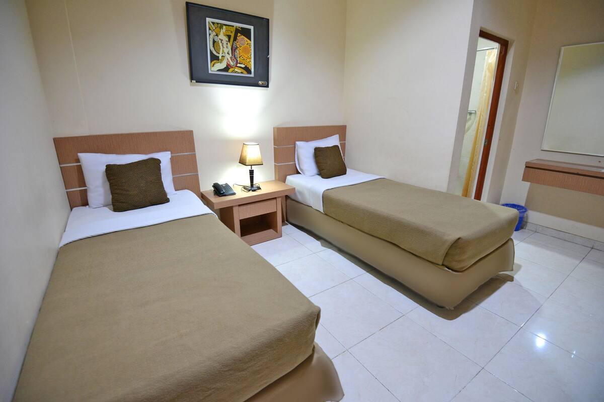 A hotel room with two beds, a nightstand, a lamp, and a painting on the wall.