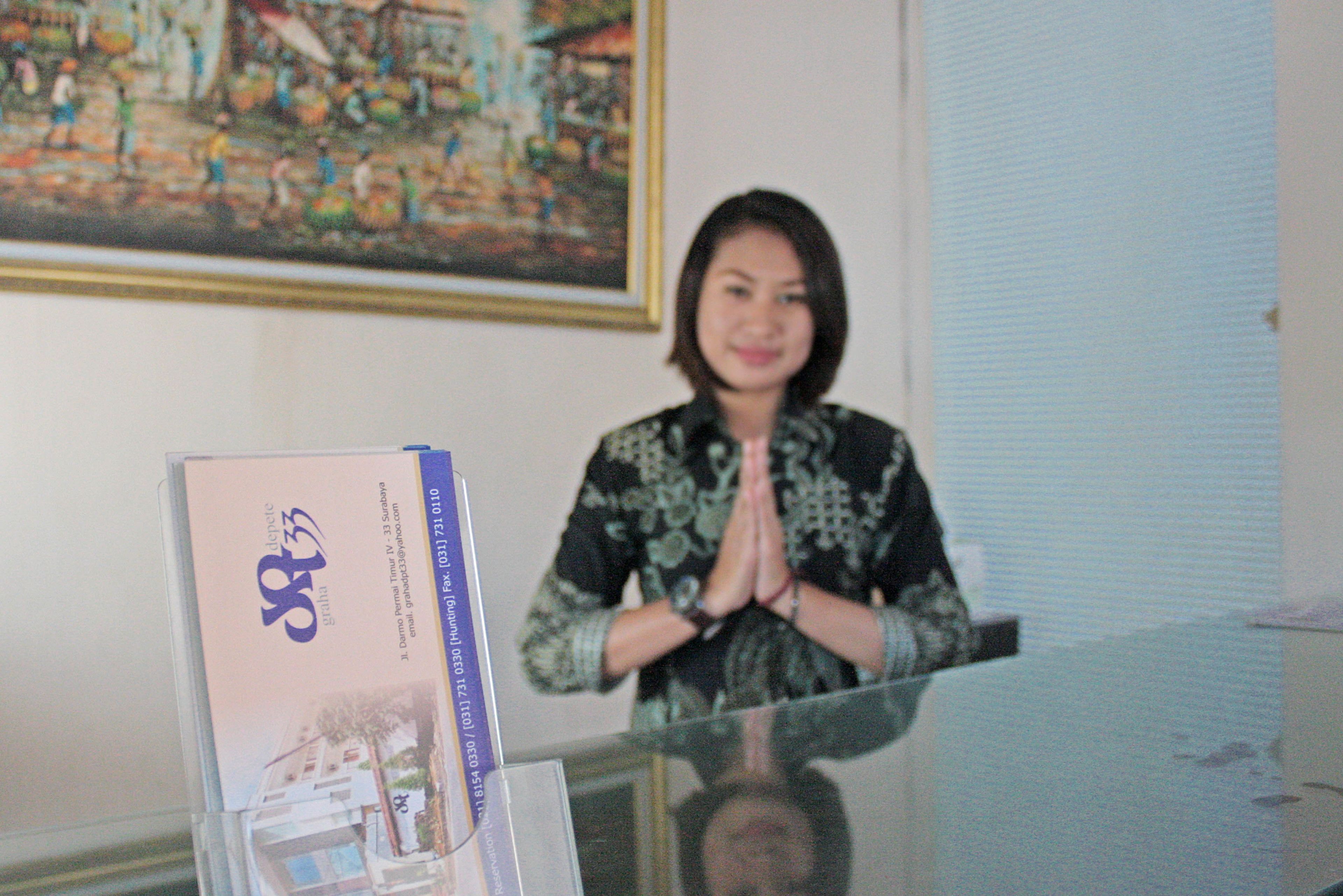 A person standing behind a glass barrier with a framed picture and a booklet on the counter.