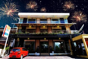 A modern hotel with a flat roof, large windows, and a red car parked in front.