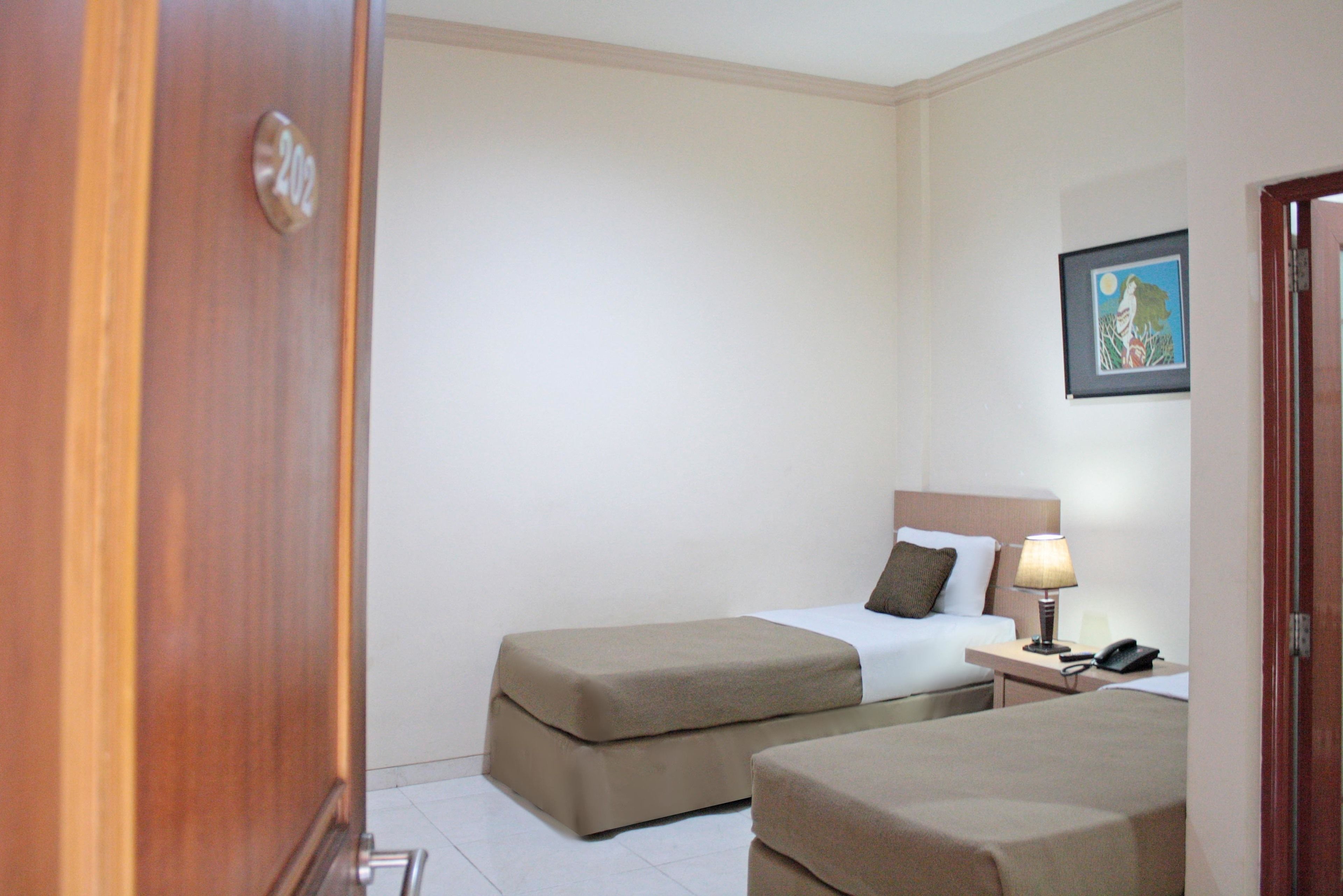 Une chambre d’hôtel avec deux lits, une table de chevet avec une lampe et un tableau encadré au mur.