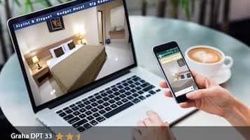 Una computadora portátil muestra una habitación con una cama, mesita de noche y un espejo. Un teléfono inteligente muestra una interfaz de reservas.