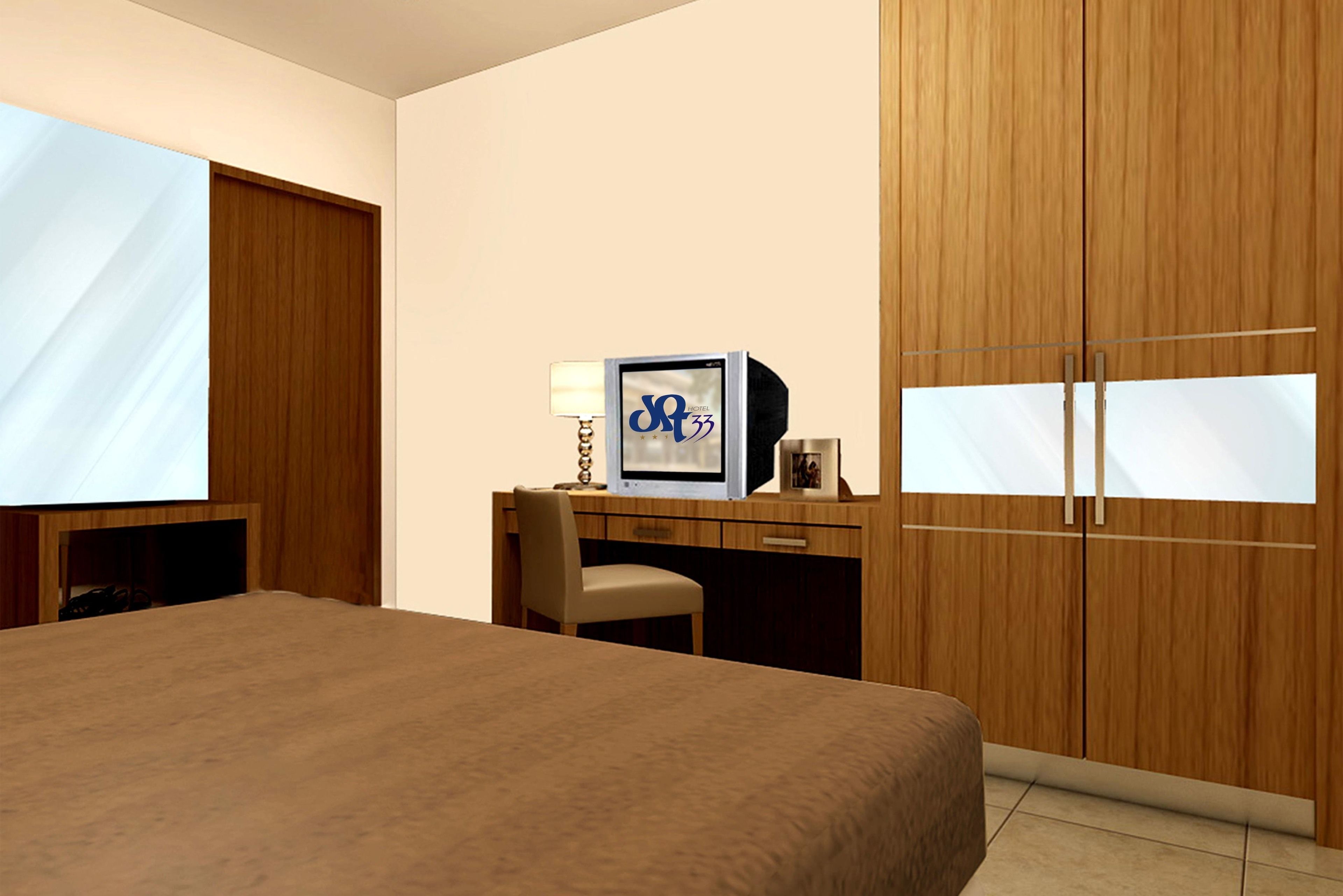 A hotel room with a large bed, a desk with a computer, a chair, and a wardrobe.