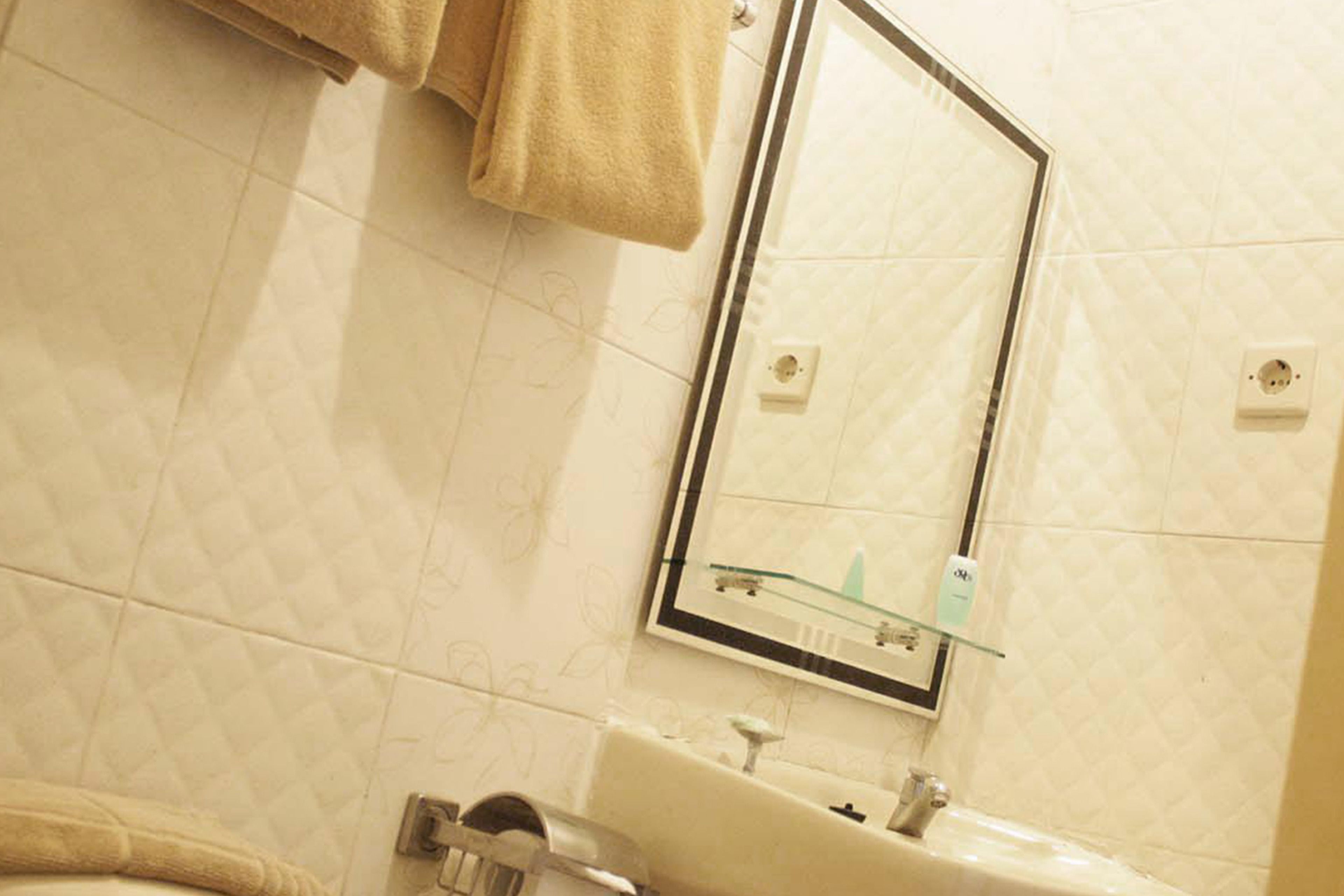 Un baño con un lavabo blanco, un estante de vidrio arriba y un espejo.