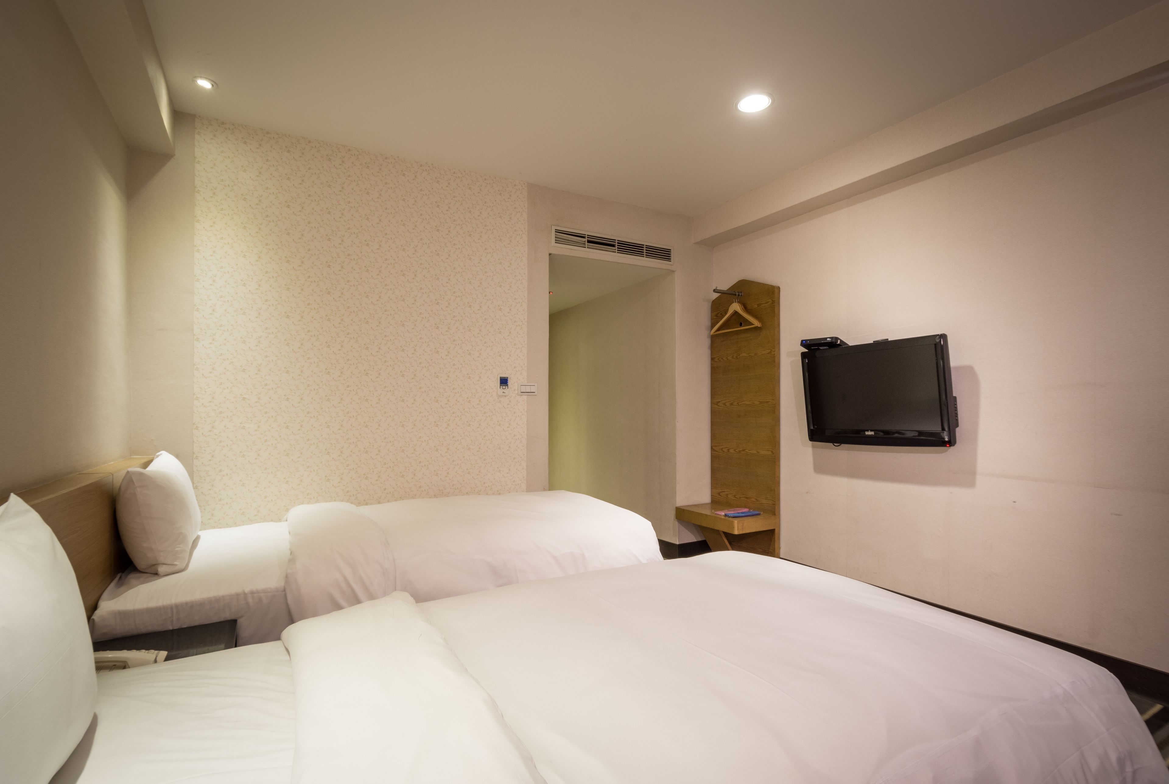 A hotel room with two beds, a television mounted on the wall, and a small table with a hanger.