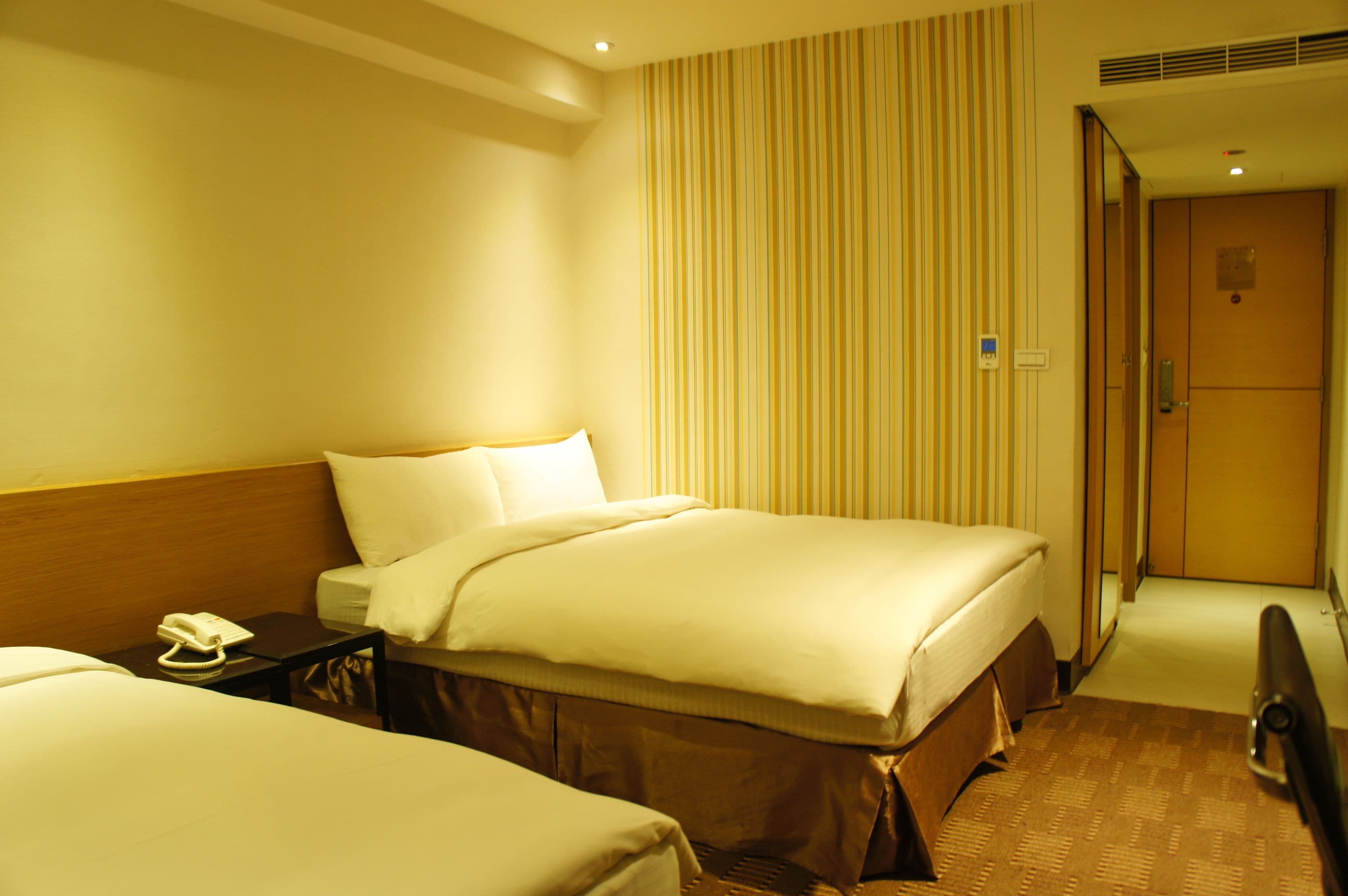 A hotel room with a bed, bedside table, and a mirror.