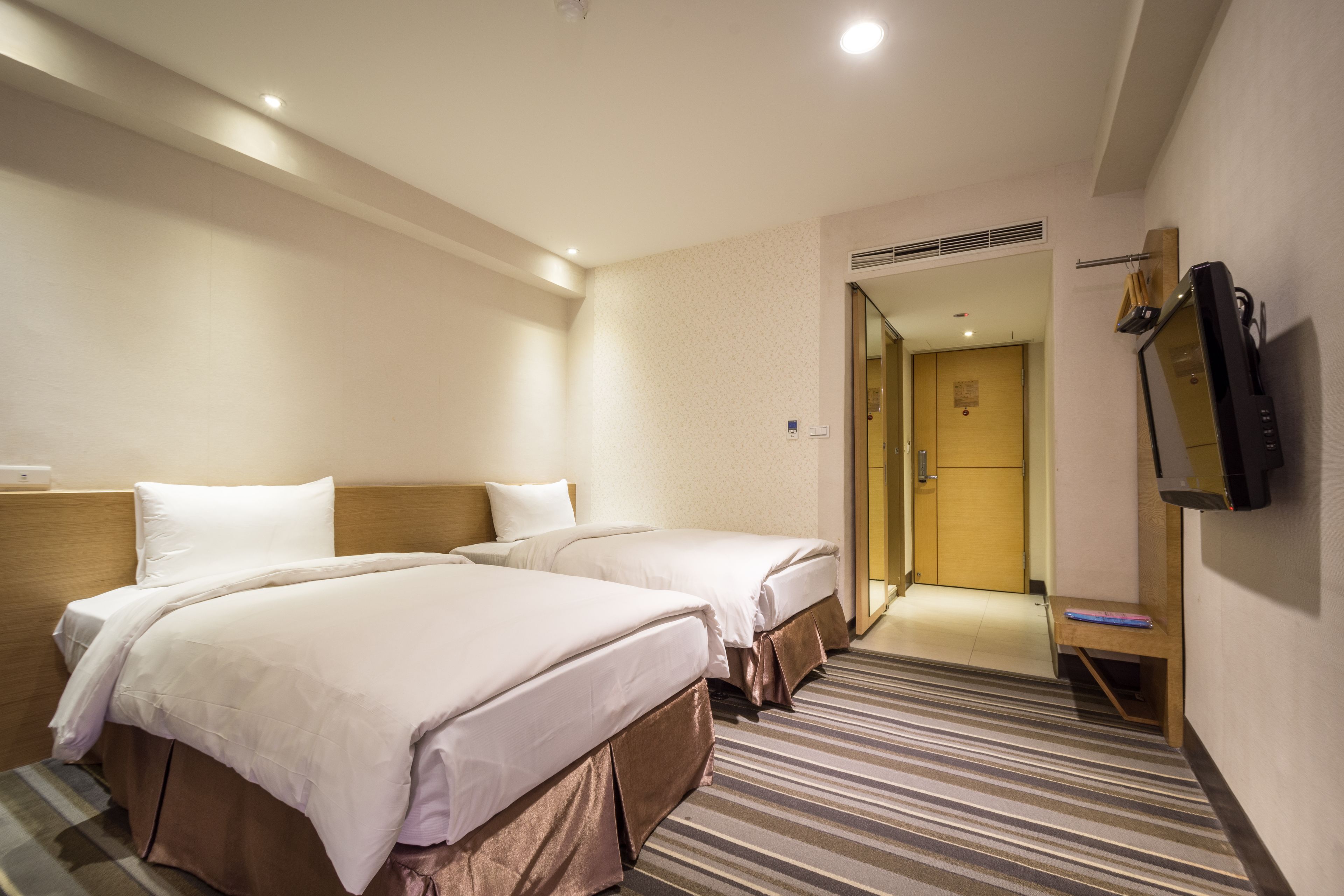 A hotel room with two beds, a TV, and a shower area.