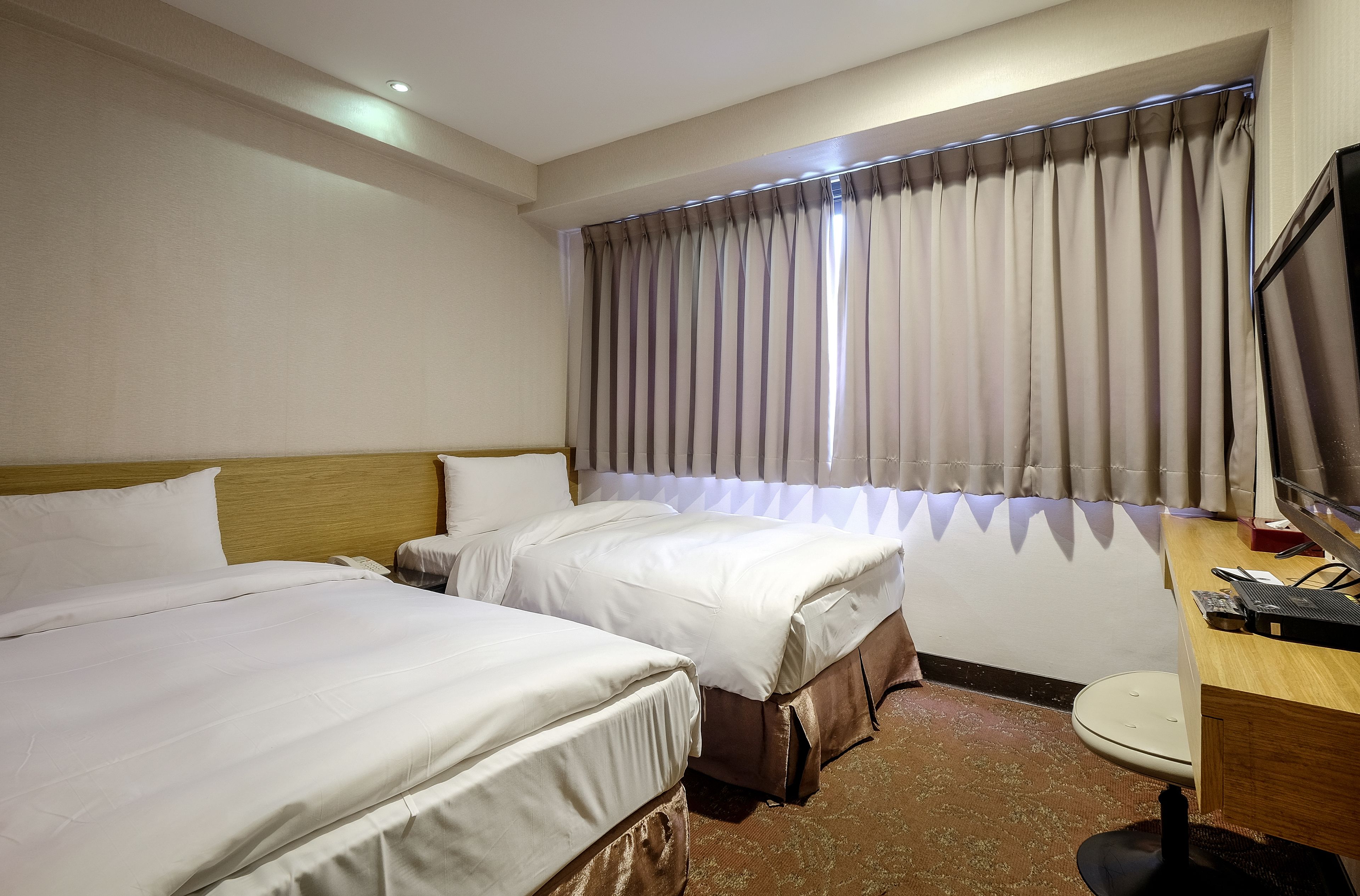 A hotel room with two beds, a desk with a computer, and a window with curtains.