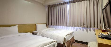 A hotel room with two beds, a desk with a computer, and a window with curtains.