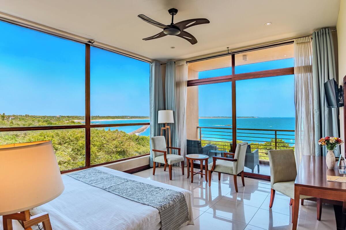 A hotel room with a large balcony, a bed, a desk, and a chair.
