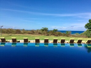 A swimming pool with lounge chairs facing the ocean, surrounded by greenery and a clear sky. - Sooriya Resort & Spa (Rekawa)