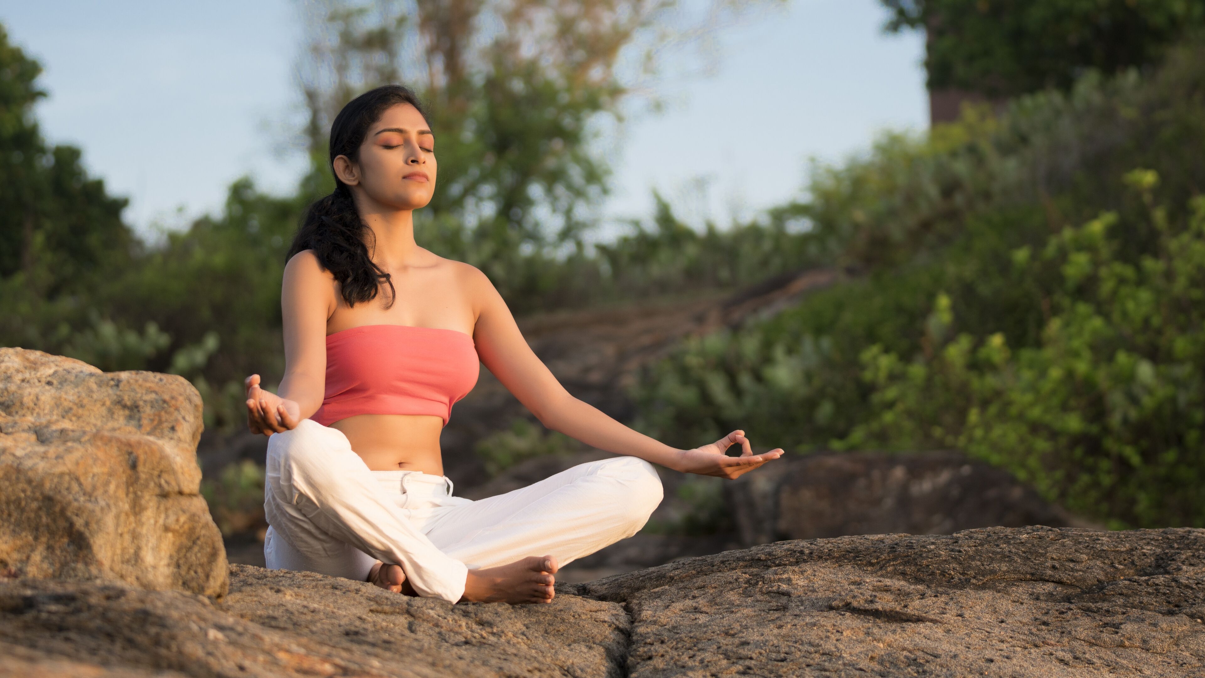 A person sitting cross-legged on a rock outdoors.