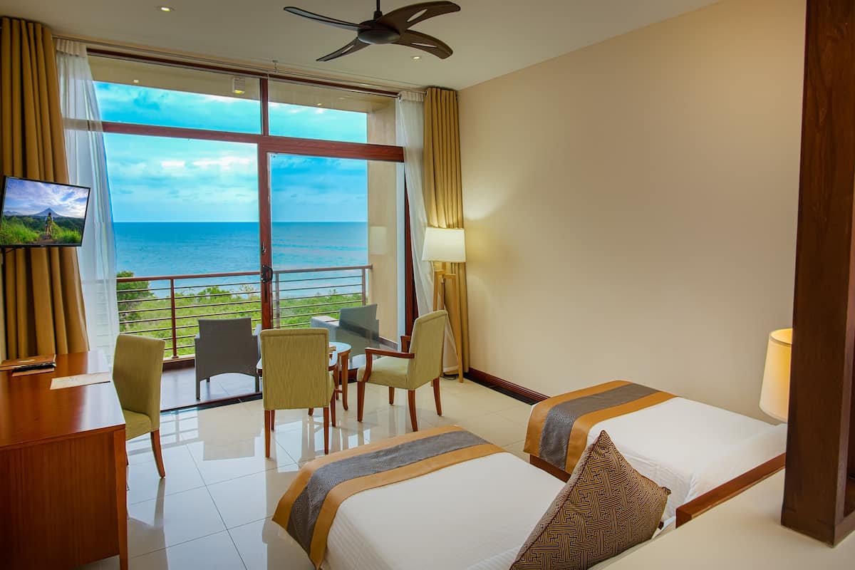 A hotel room with a bed, a desk, a chair, a TV, and a view of the ocean.