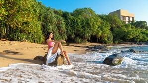 A person sitting on a rock by the sea, with a building in the background. - Sooriya Resort & Spa (Rekawa)