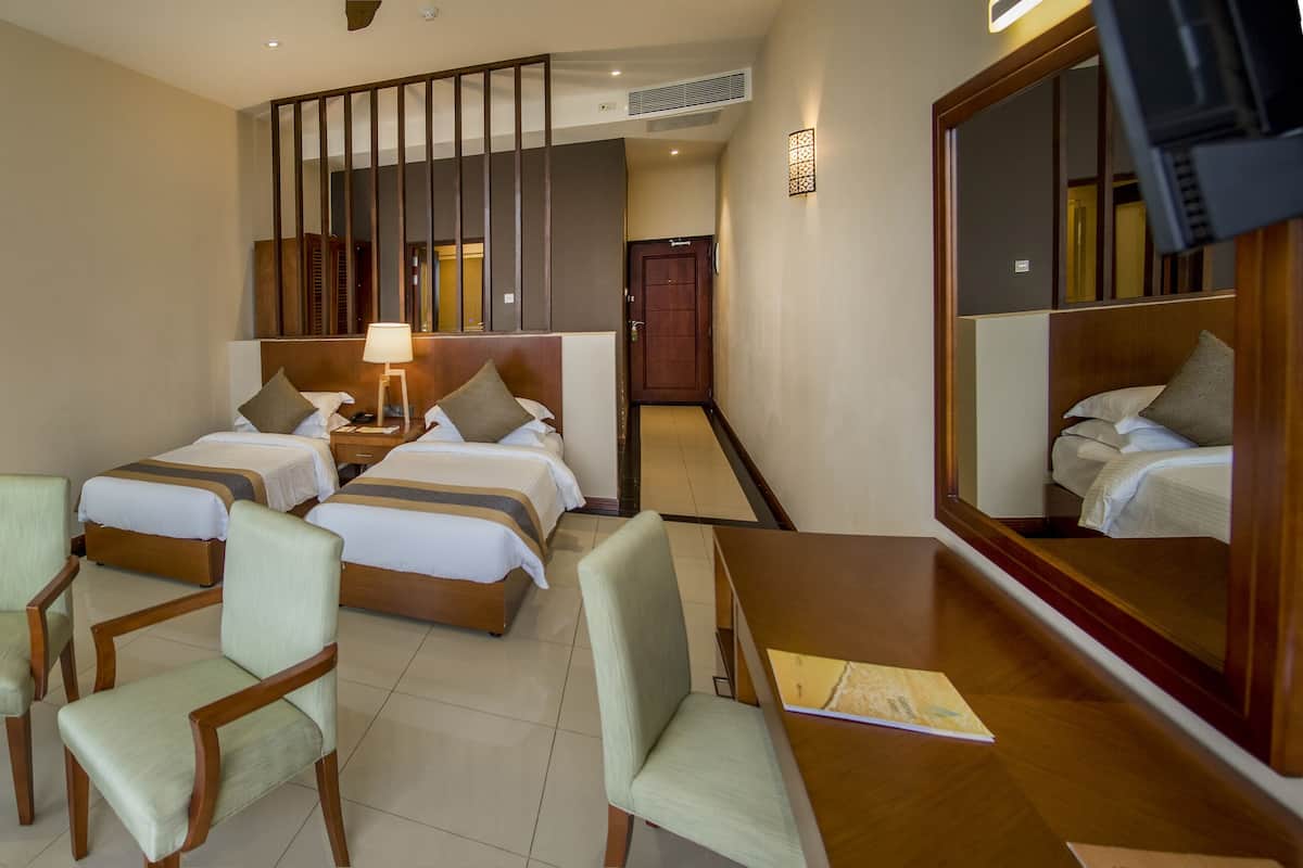A hotel room with two beds, a sitting area with chairs, a small table, a lamp, and a mirror.