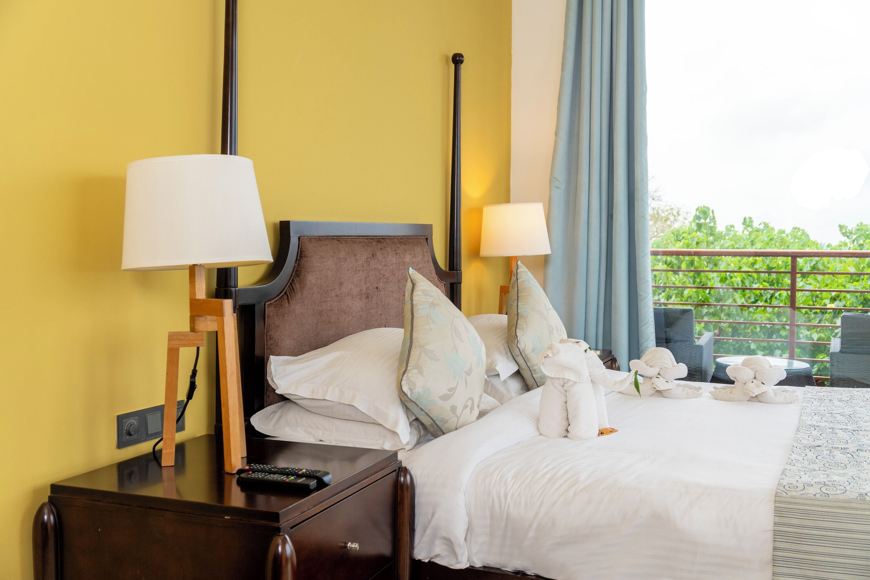 Habitación de hotel con cama, lámparas de noche, mesita de noche, control remoto y vistas a zonas verdes.