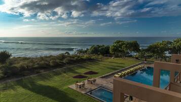 A pool area with a view of the ocean, surrounded by greenery and a clear sky.