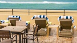 A beachside terrace with wooden tables and chairs, a white towel with "Sofitel" embossed on it, and a view of the ocean. - Sooriya Resort & Spa (Rekawa)
