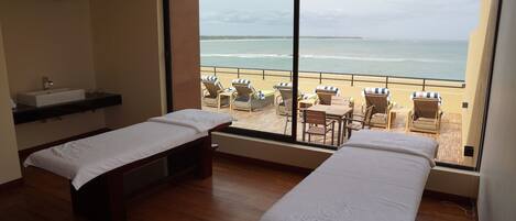 A room with two beds, a window with a view of the beach, and a small table with chairs.