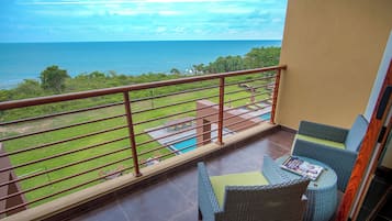 A balcony with a view of the ocean, a pool, and outdoor furniture.