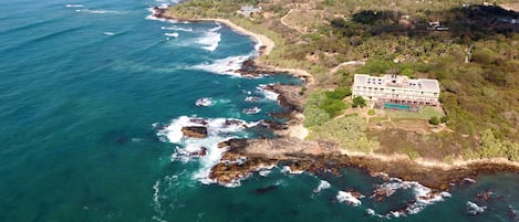 An aerial view of a coastal property with a large building, a beach, and rocky coastline.