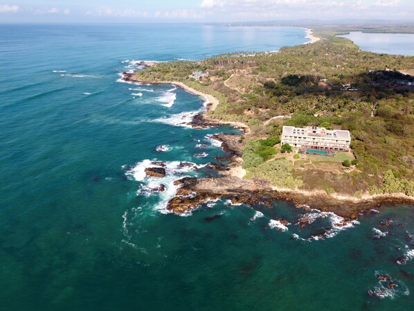 An aerial view of a coastal property with a large building, a beach, and rocky coastline. - Sooriya Resort & Spa (Rekawa)