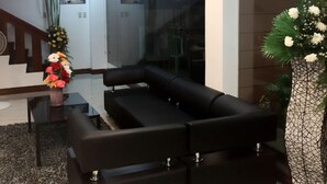 Uma sala de estar moderna com um sofá preto, divisória de vidro e um vaso decorativo com flores.