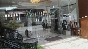 Entrada de hotel com porta de vidro, um candelabro, área de estar externa e um carro estacionado dentro.