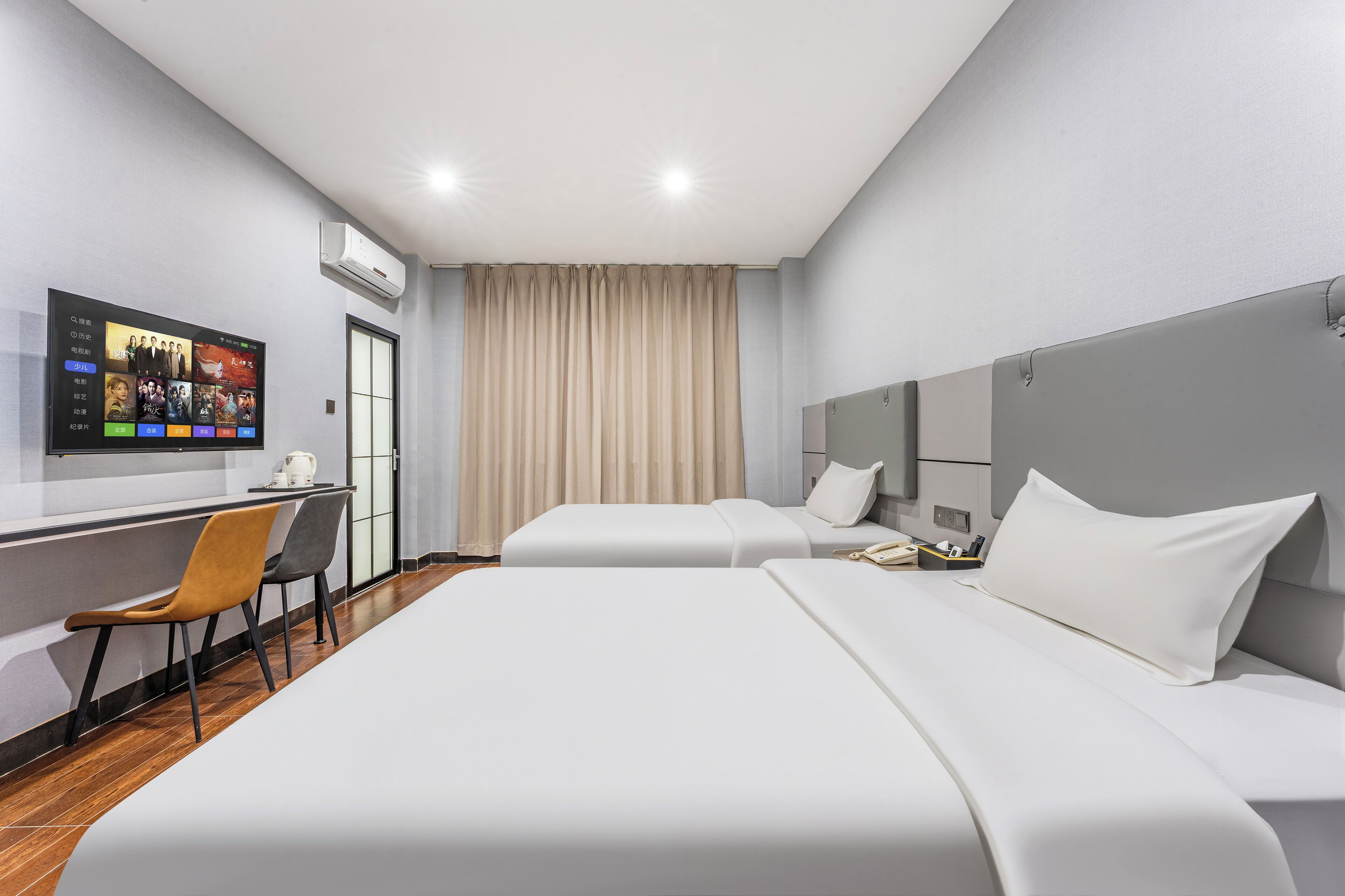 Une chambre d’hôtel avec deux lits, un bureau avec une chaise, un téléviseur fixé au mur et un appareil de climatisation.