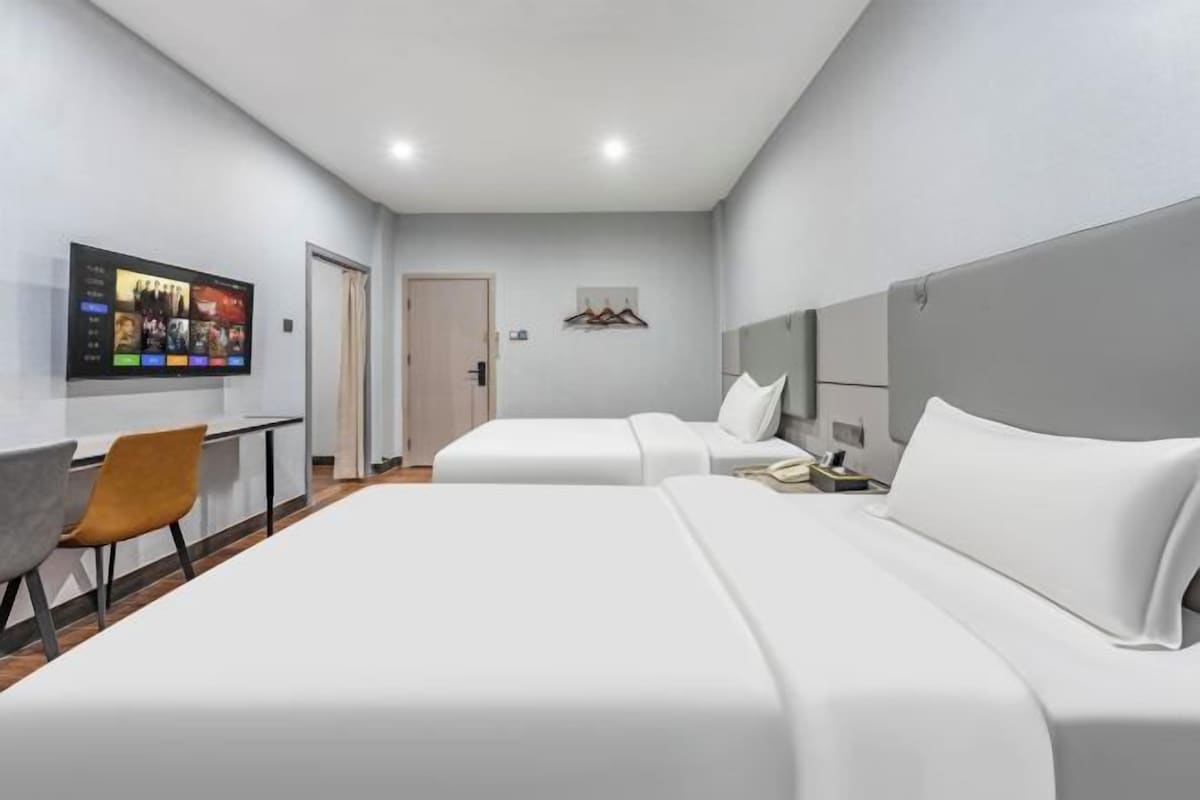 A hotel room with two beds, a desk, and a TV mounted on the wall.