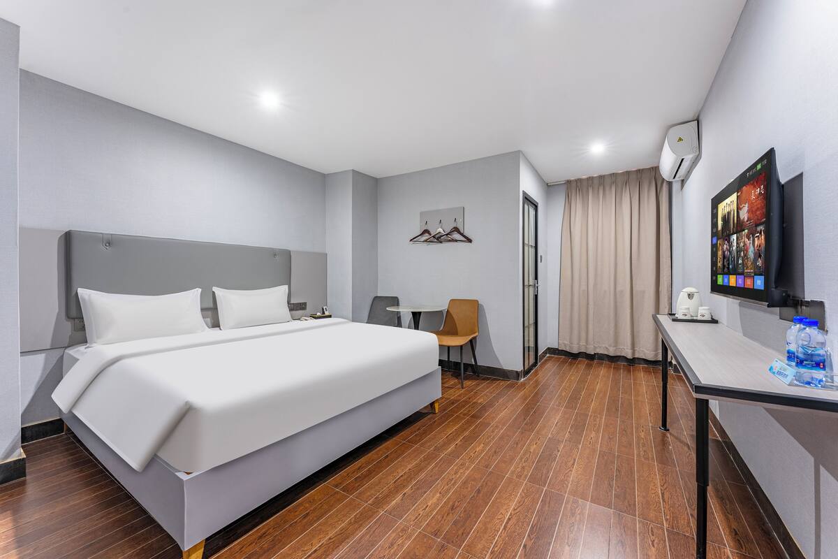 Quarto de hotel com uma cama grande, uma escrivaninha com cadeira, televisão e ar condicionado fixado na parede.