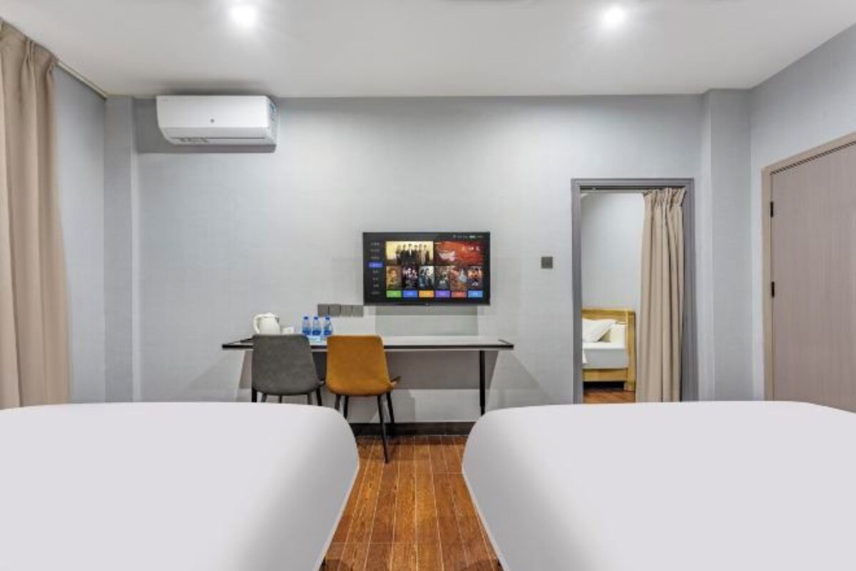 A hotel room with two beds, a desk with a computer, a TV, and an air conditioning unit.