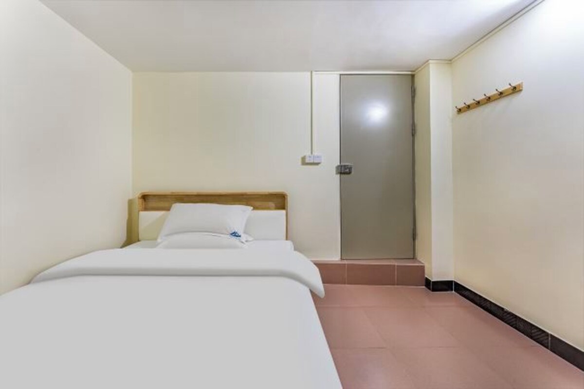 A small, clean room with a bed, a door, and a wall-mounted hook.