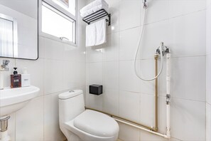 Un baño con lavamanos blanco, inodoro y ducha con cabezal de ducha manual.