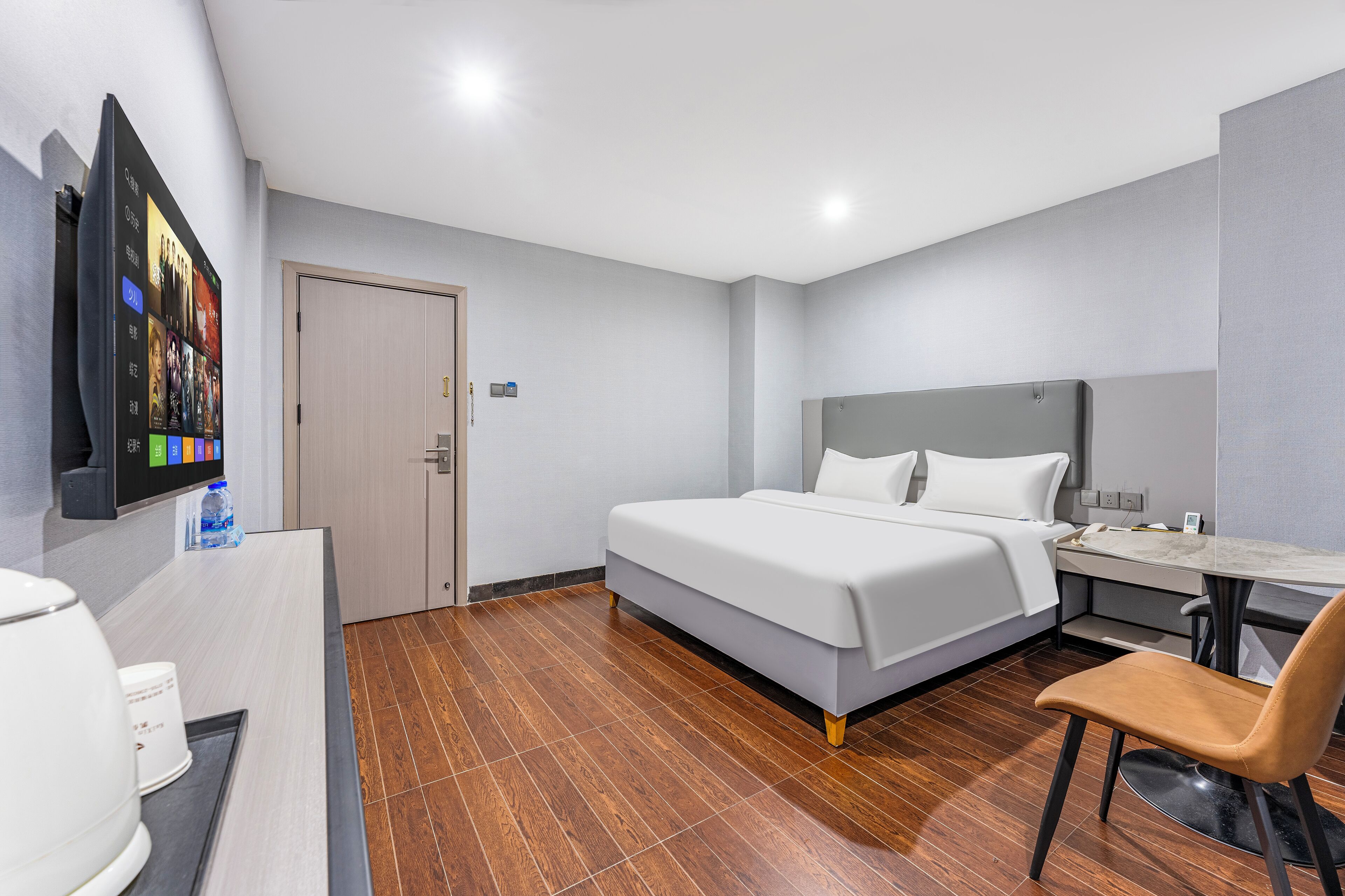Ein Hotelzimmer mit einem Bett, einem Schreibtisch, einem Stuhl, einem an der Wand montierten Fernseher und einem Holzboden.