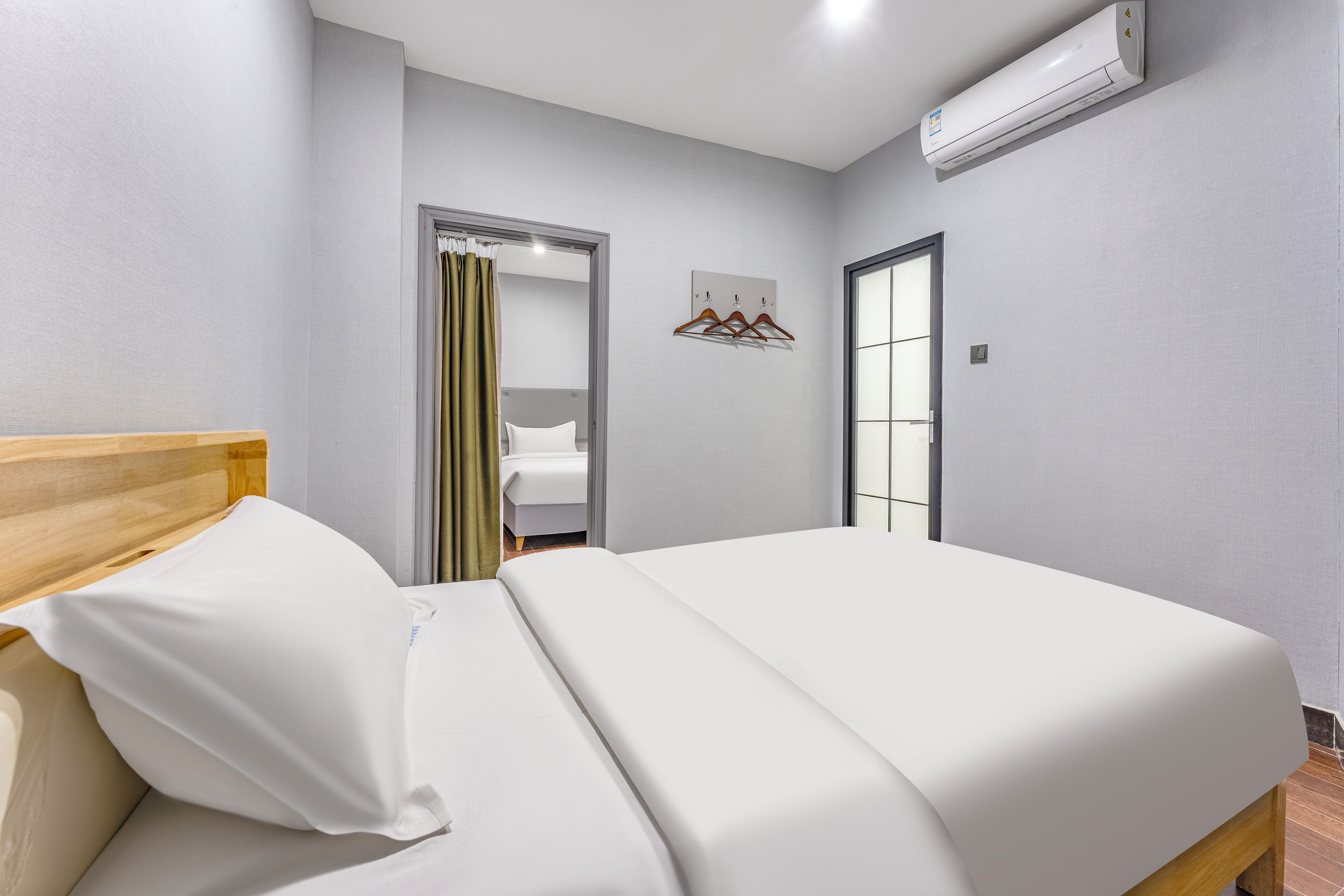 Una habitación de hotel con una cama, cabecera de madera, ventana con vistas y unidad de aire acondicionado.