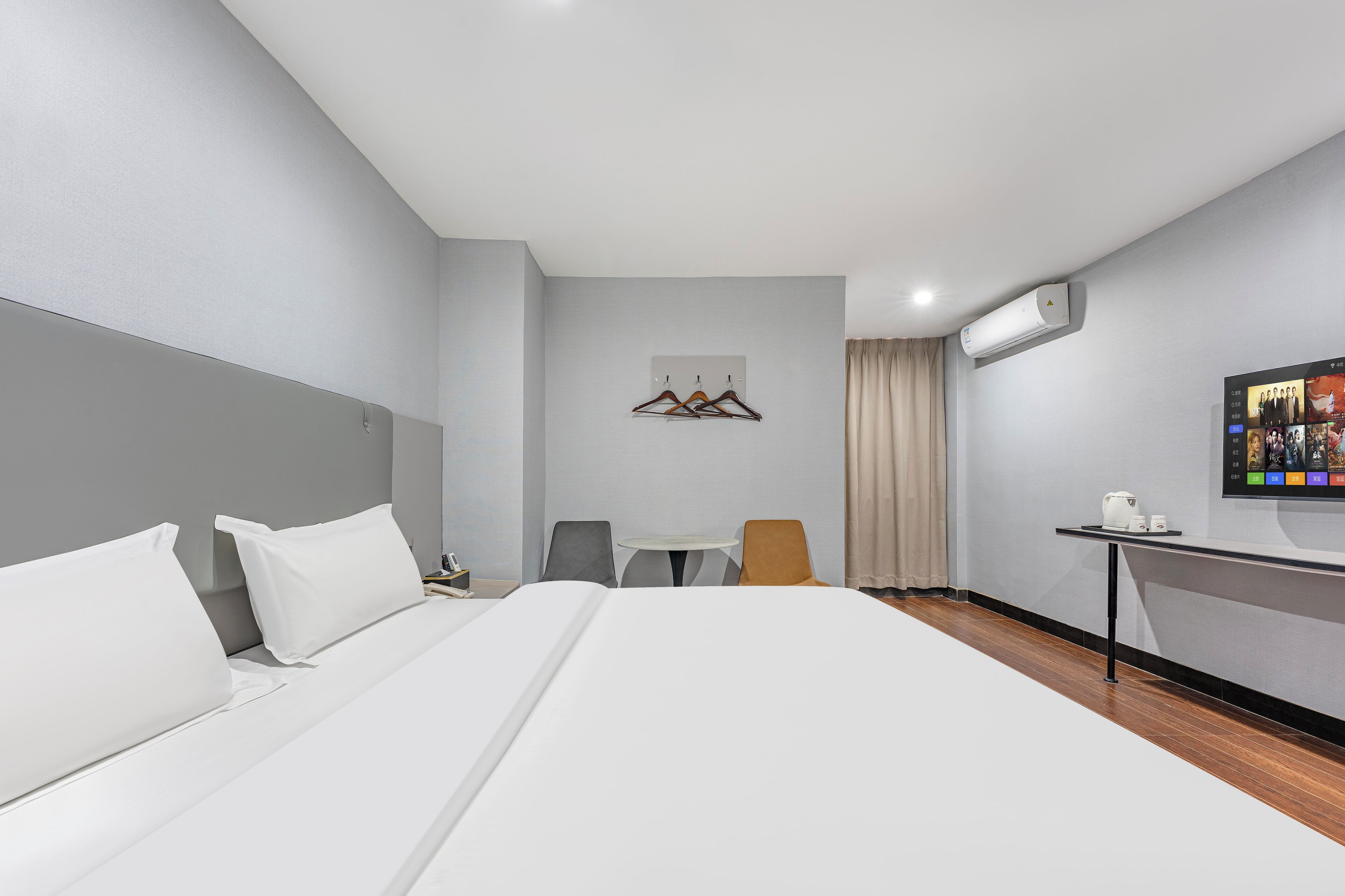 A hotel room with a bed, a small table with a kettle, a TV, and a coat rack.