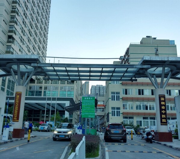 A hospital entrance with a covered walkway, multiple cars, and a clear sky. - Kaixin Express Hotel (Shenzhen)