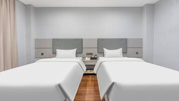 A hotel room with two single beds, a nightstand, a lamp, and a small table.