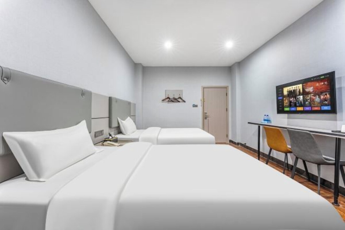 A hotel room with two beds, a desk with a chair, a TV, and a door.