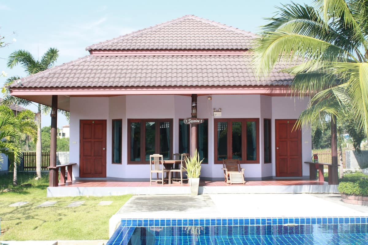 Uma casa de dois andares com telhado de telhas, piscina e um pátio com cadeiras e mesa.