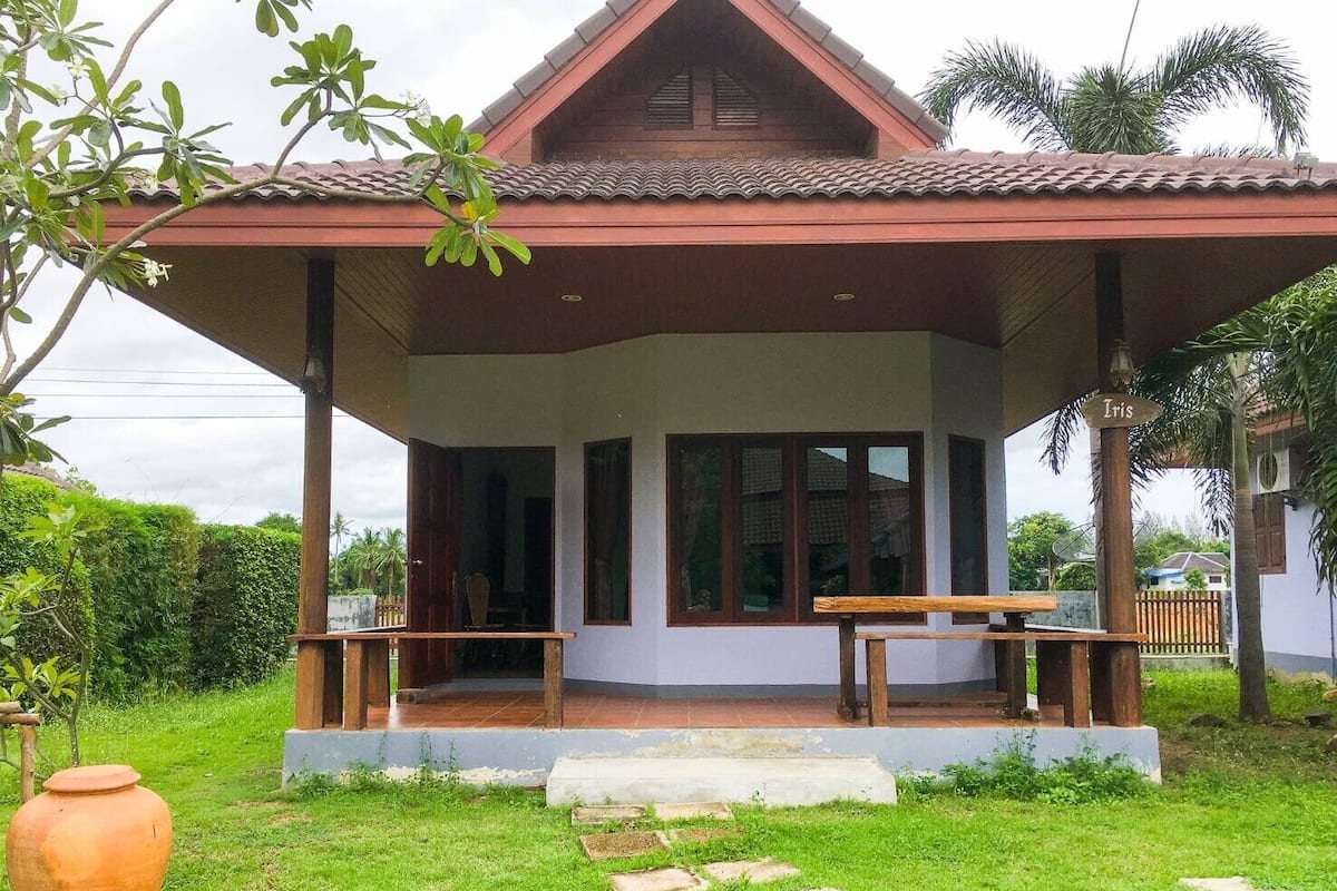 Uma casa com varanda coberta, um banco de madeira e um grande vaso de terracota.