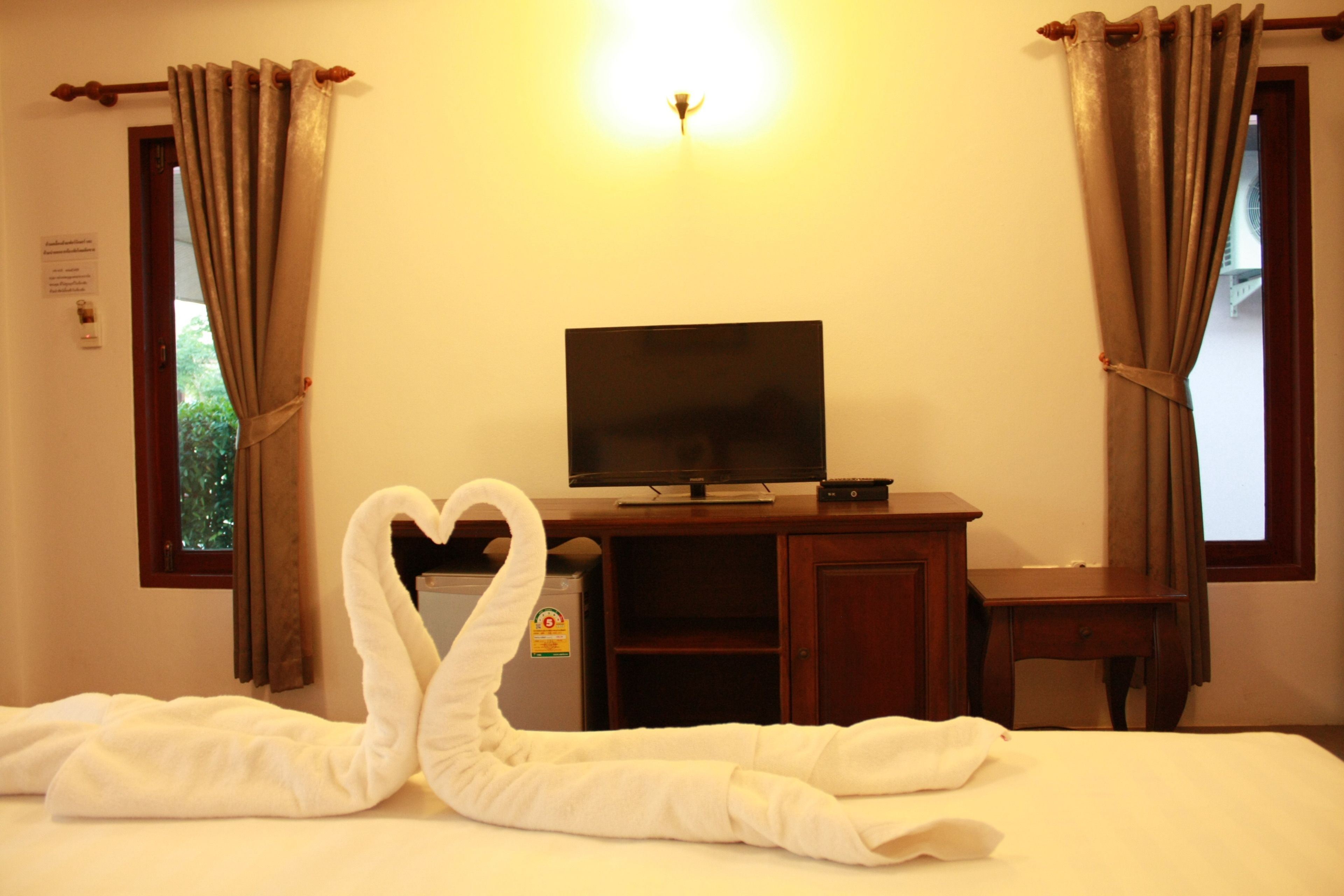 A hotel room with a bed, a television on a wooden stand, and curtains on the windows.