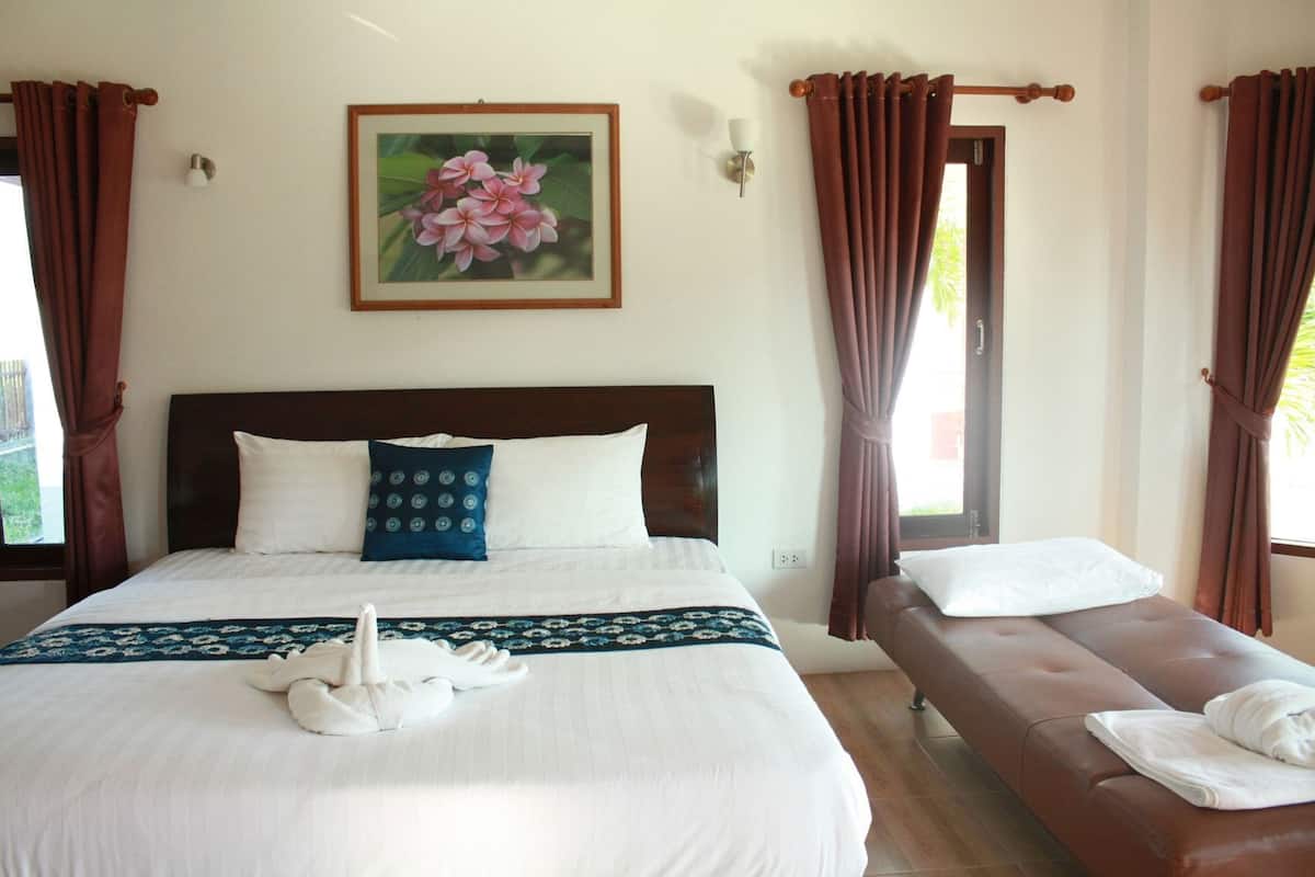 Quarto de hotel com uma cama grande, um sofá menor, uma obra de arte floral emoldurada e cortinas.