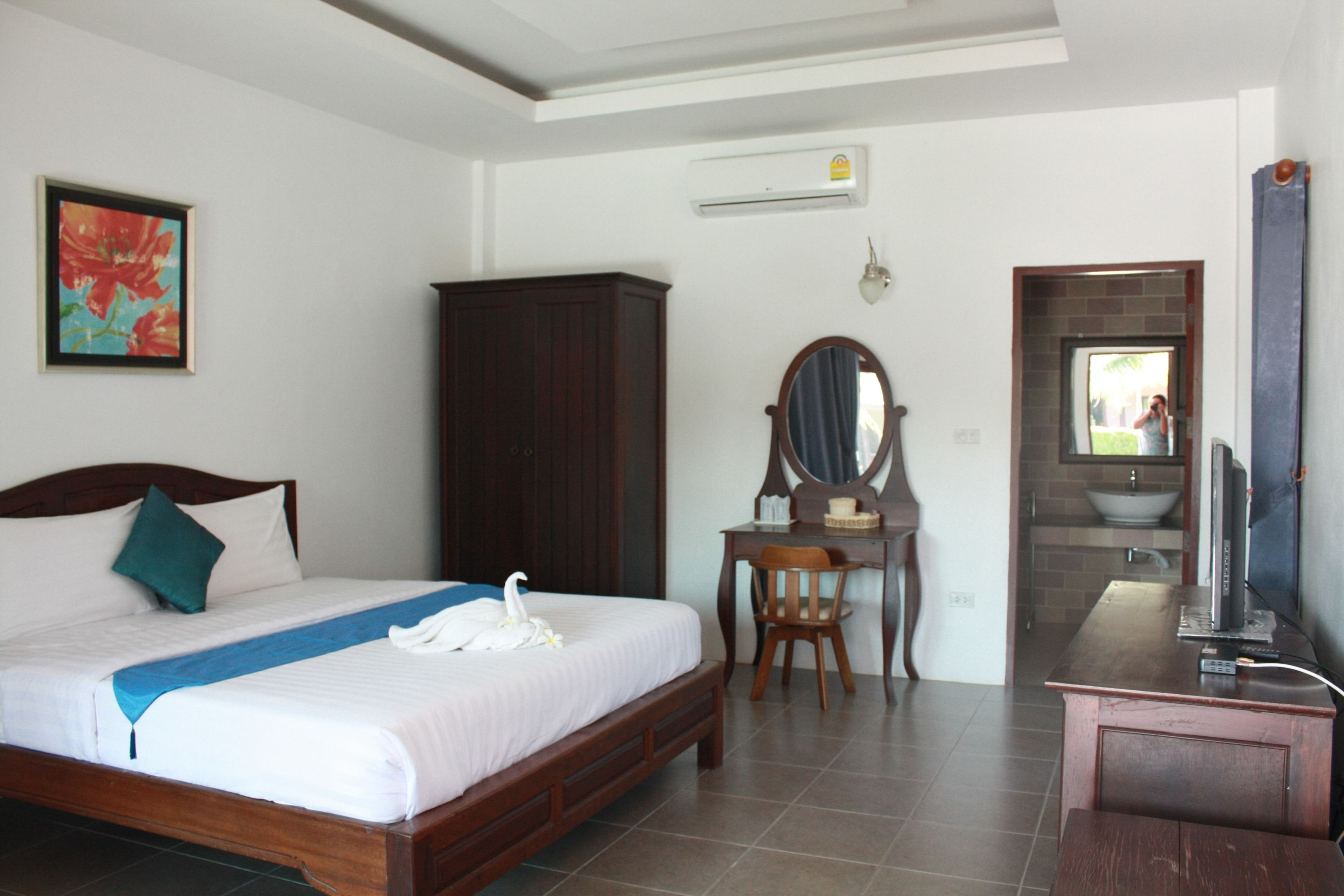 A hotel room with a bed, a desk, a mirror, a TV, and a bathroom visible through an open door.