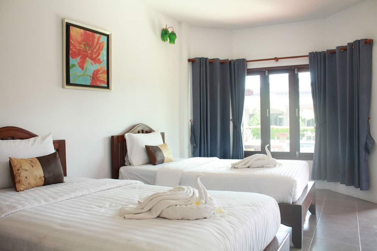 Quarto de hotel com duas camas, um quadro, um adorno verde na parede e vista pela janela.