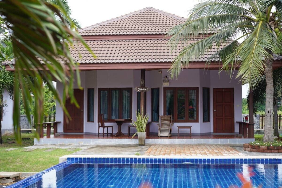 Um edifício de dois andares com telhado de telhas, piscina e varanda coberta com área de estar.