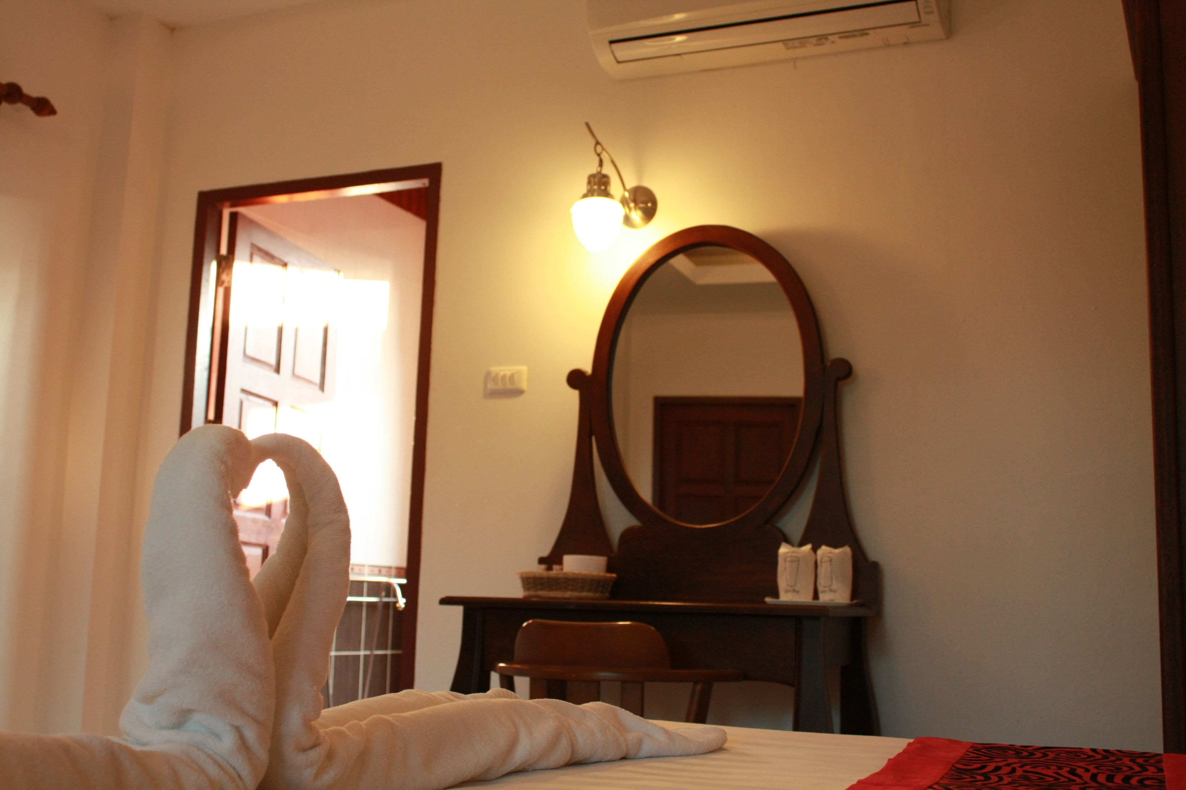 A hotel room with a bed, a desk with a mirror, and an air conditioning unit on the wall.