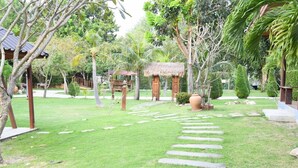 A well-maintained garden with a stone pathway leading to a thatched-roof structure. - Waterside Resort (Pranburi)