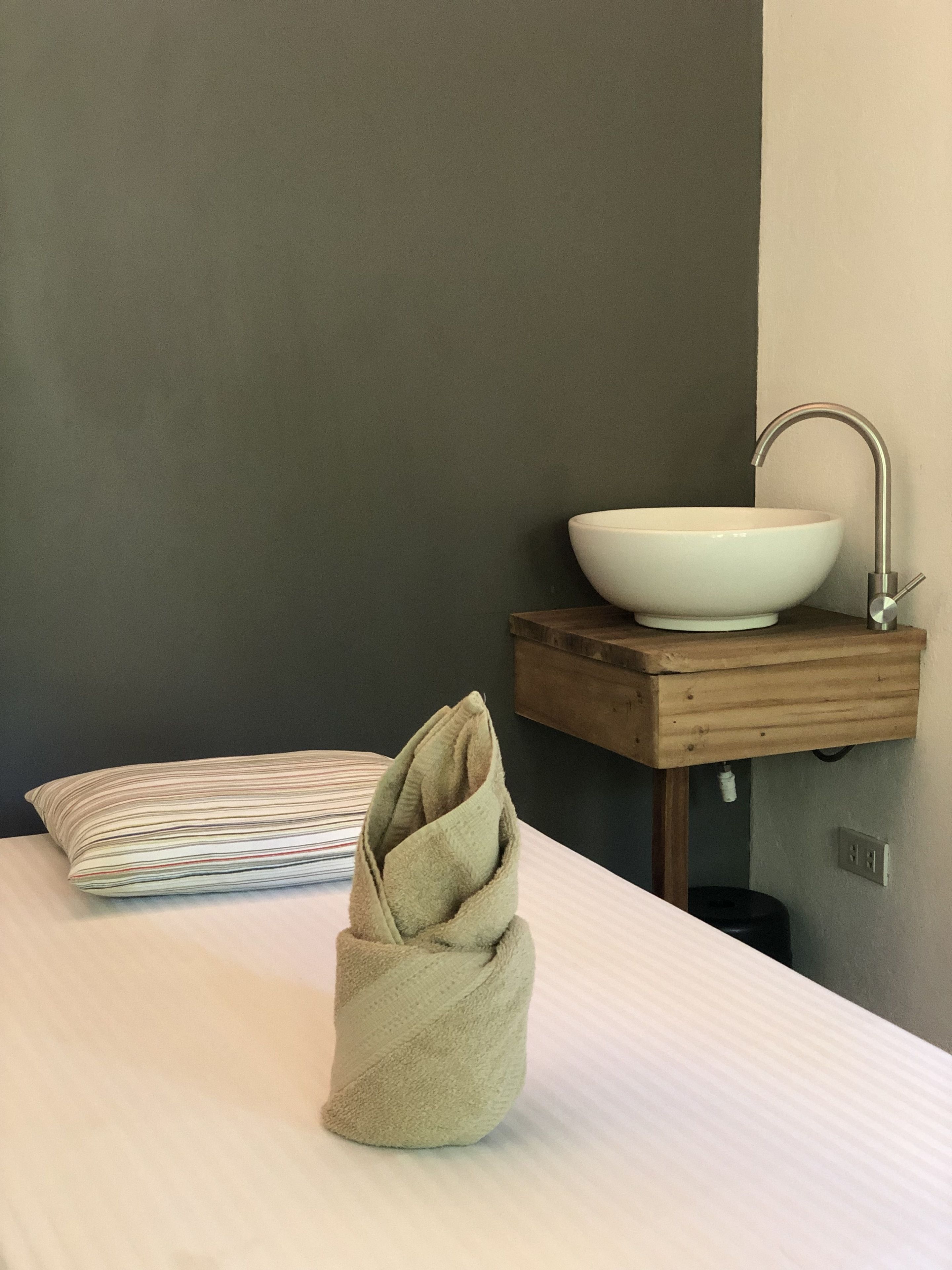 Une salle de bain avec un lavabo blanc posé sur un meuble en bois, une serviette sur le lit et un coussin à rayures.